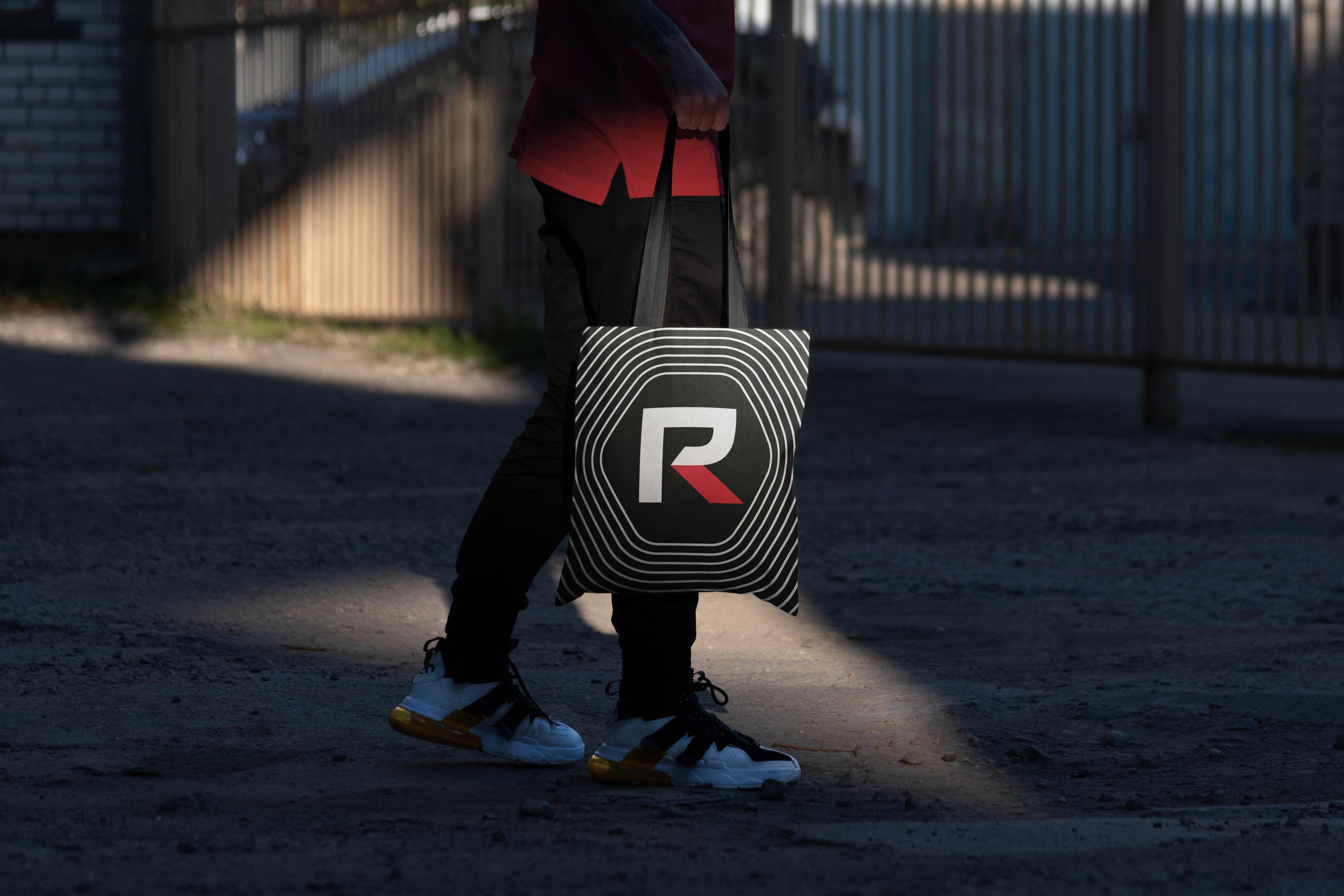 Person carrying a black tote bag printed with the RevolutionParts R logo
